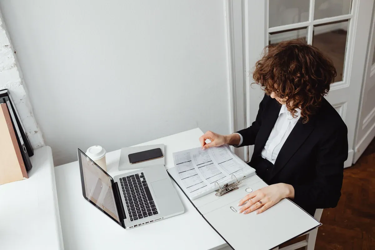 A professional reviewing a binder of account documents beside a laptop before funding a forex account