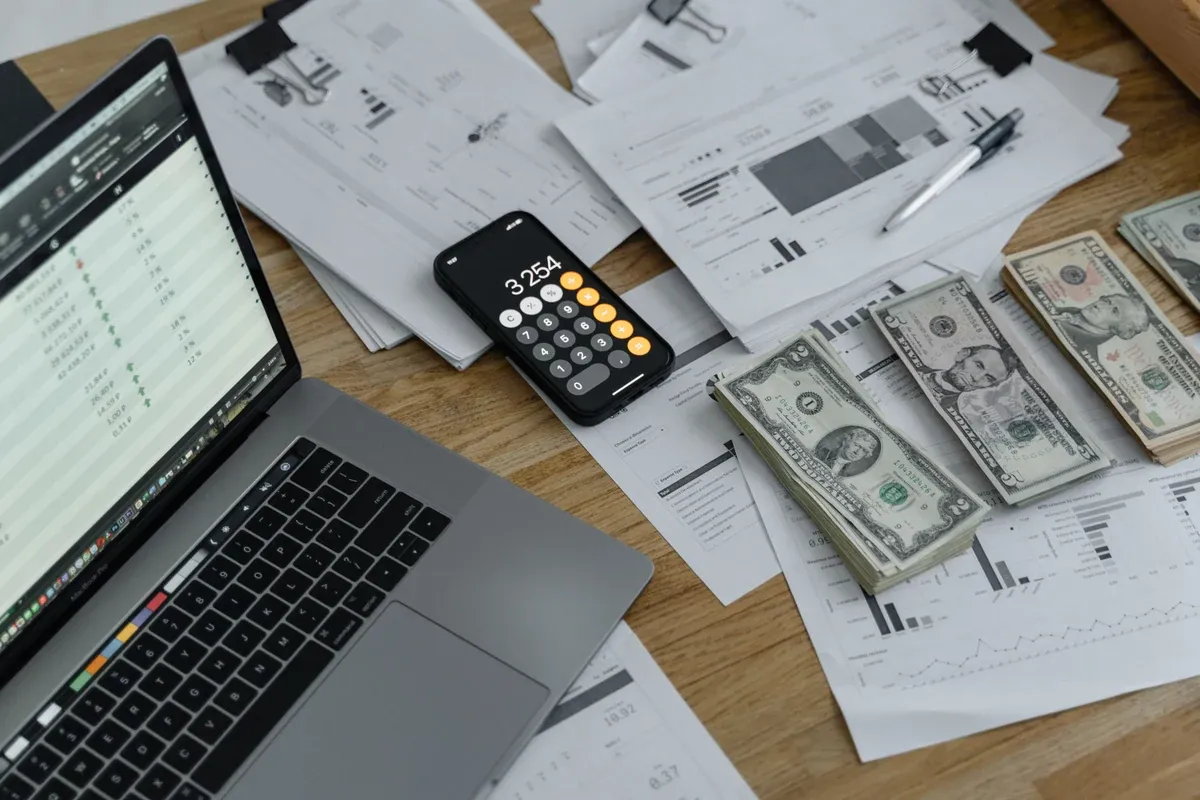 US dollar bills beside financial statements and a laptop, with cash kept separate from the paperwork